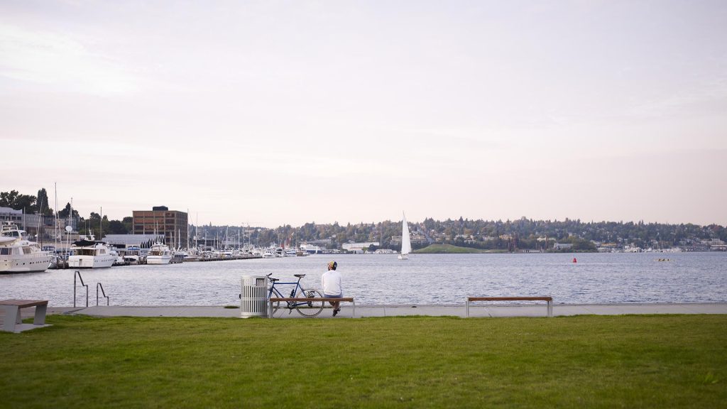 Man with bicycle sitting on bench looking at Lake Union